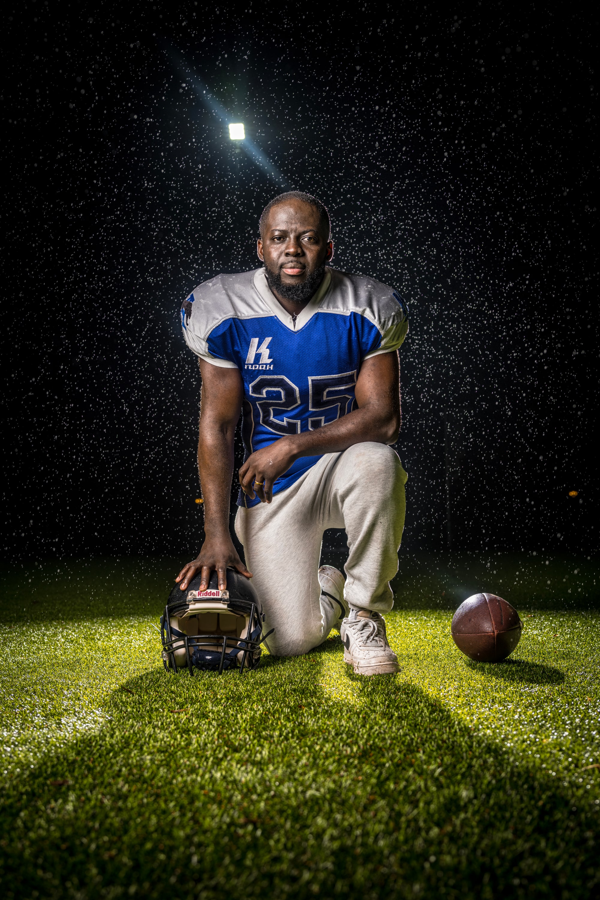 Godwin Arhin knielt in american football tenue op een sportveld in de regen, met een hand op zijn helm