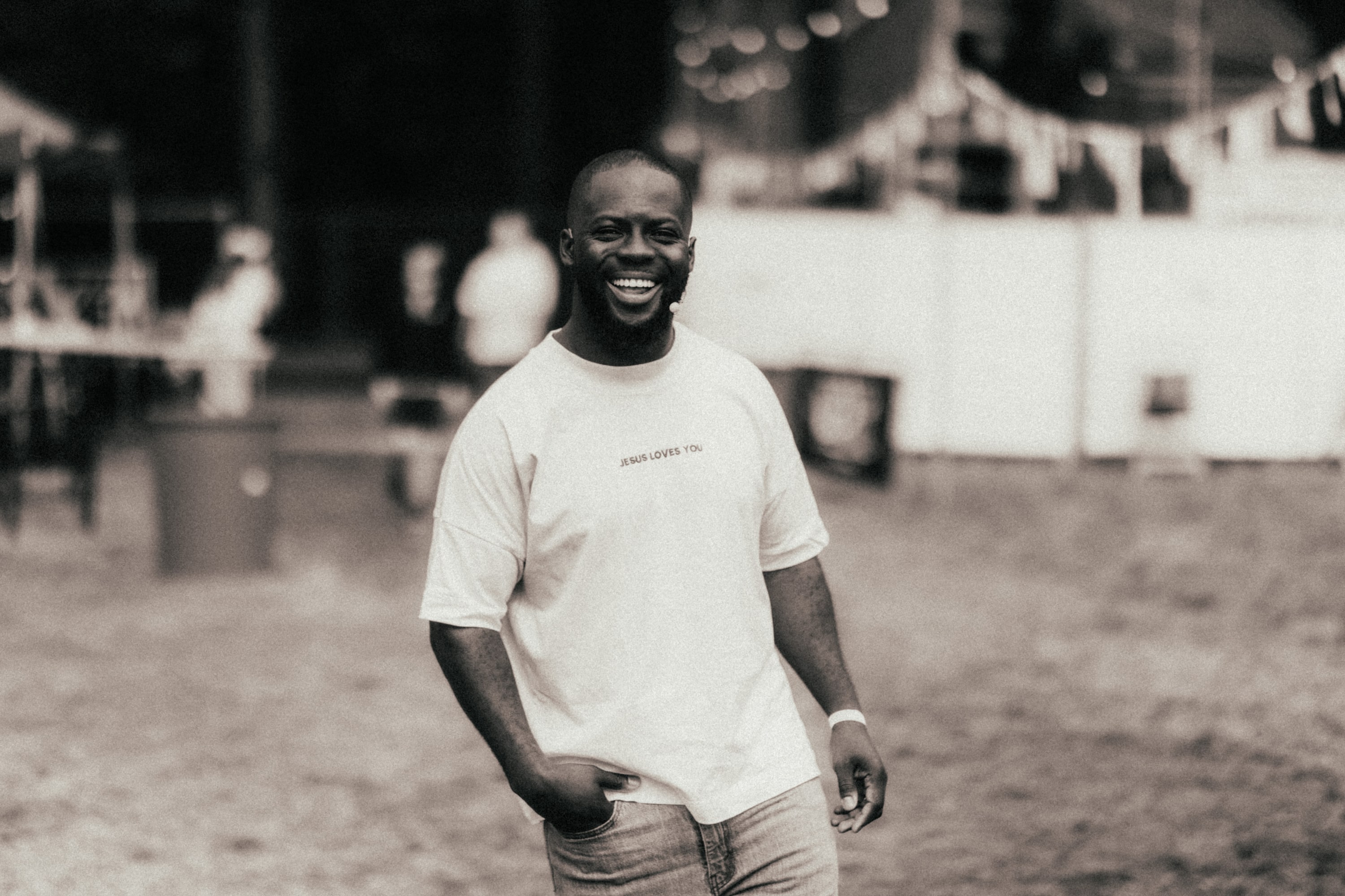 Godwin Arhin loopt lachend over een festivalterrein met een hand in zijn zak, foto in sepia