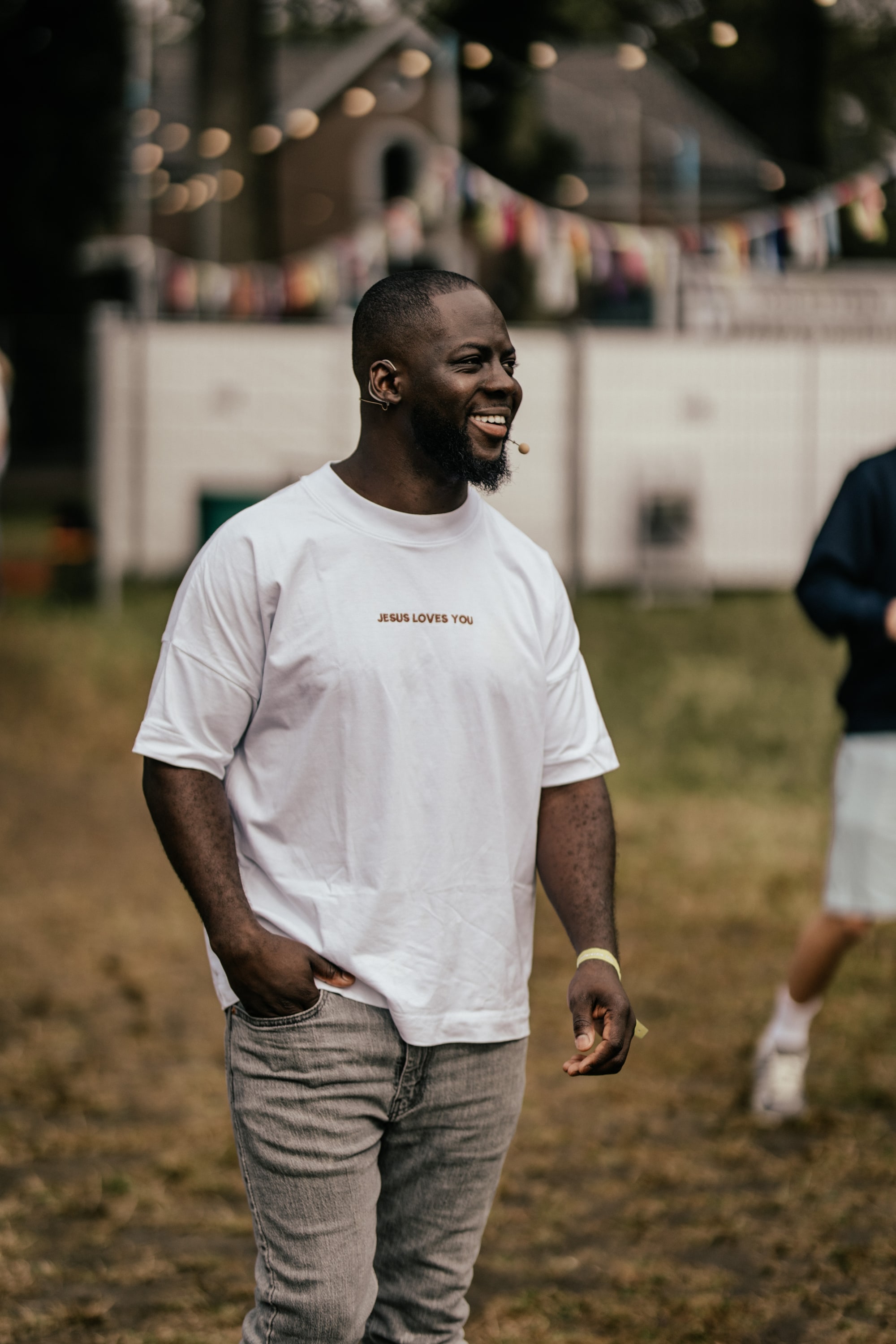 Godwin Arhin met headsetmicrofoon op een festivalterrein, lachend in een wit shirt