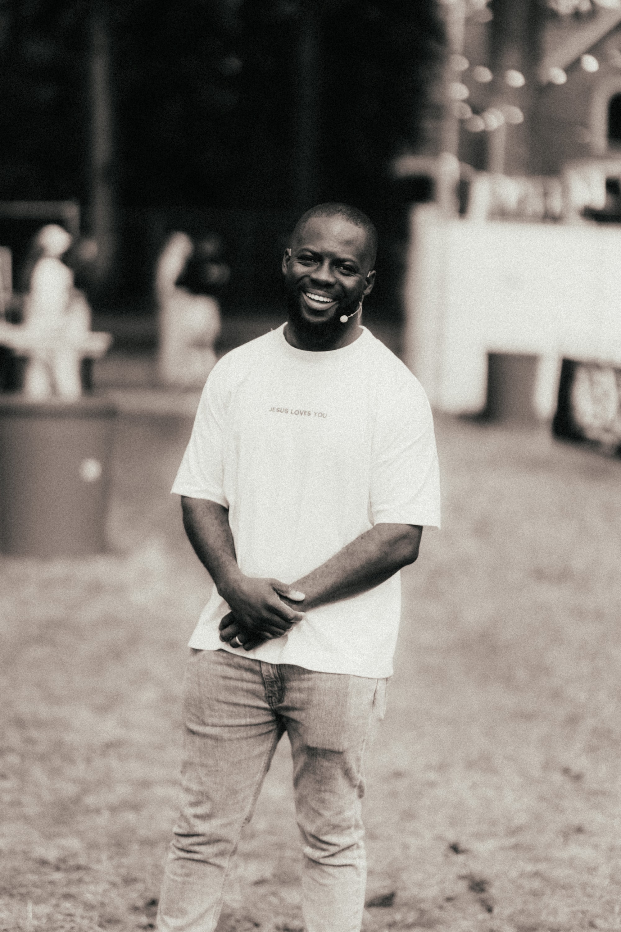 Godwin Arhin staat lachend op een festivalterrein, handen gevouwen, foto in sepia
